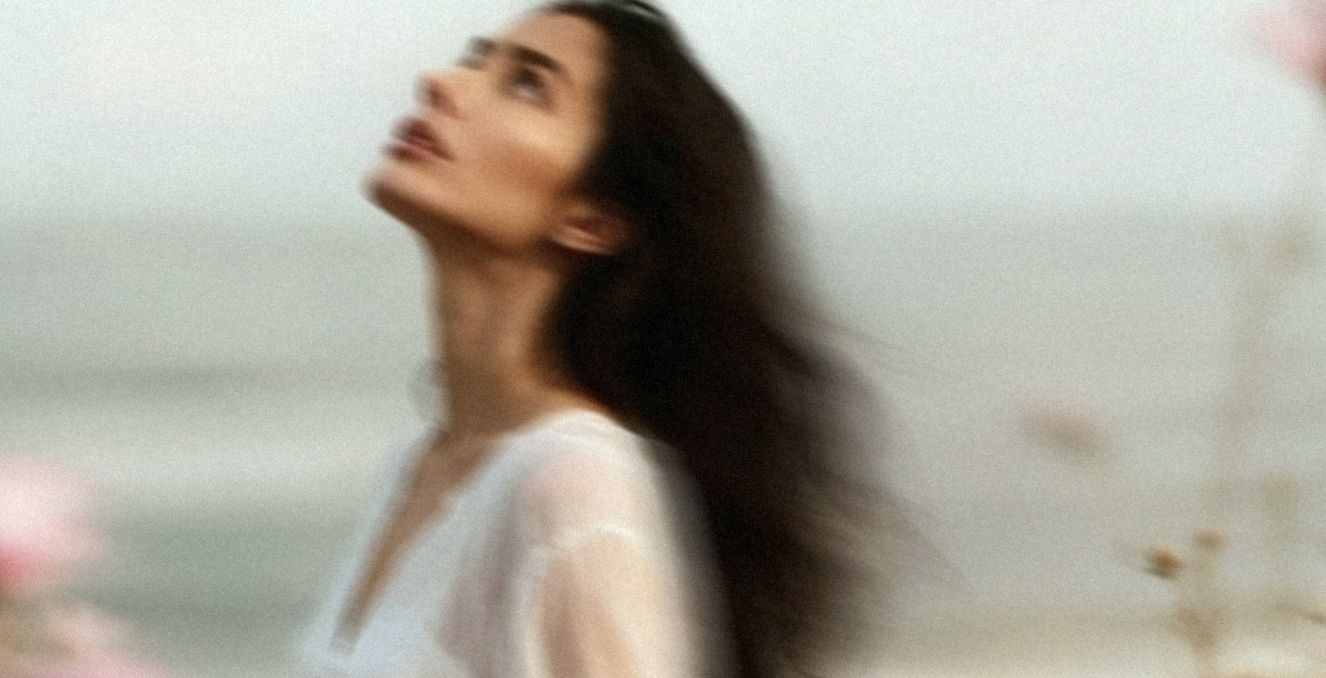 Soft-focus portrait of a woman looking upward beside the sea.