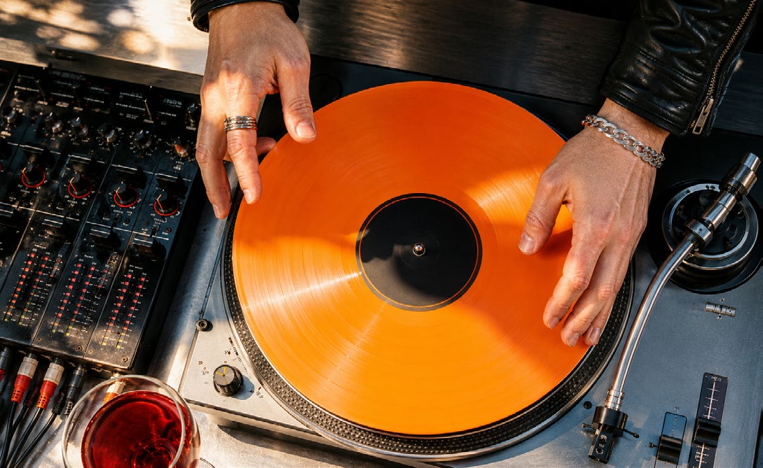DJ placing an orange vinyl record on a turntable.